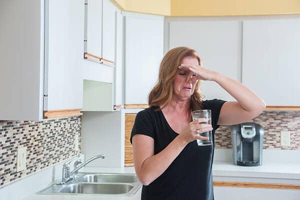 Water Conditioning | Woman holding a glass of water while pinching her nose.