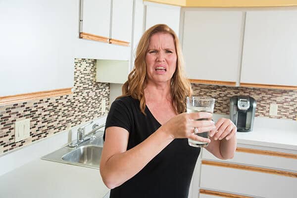 Water Conditioning | Woman holding a glass of water while wincing